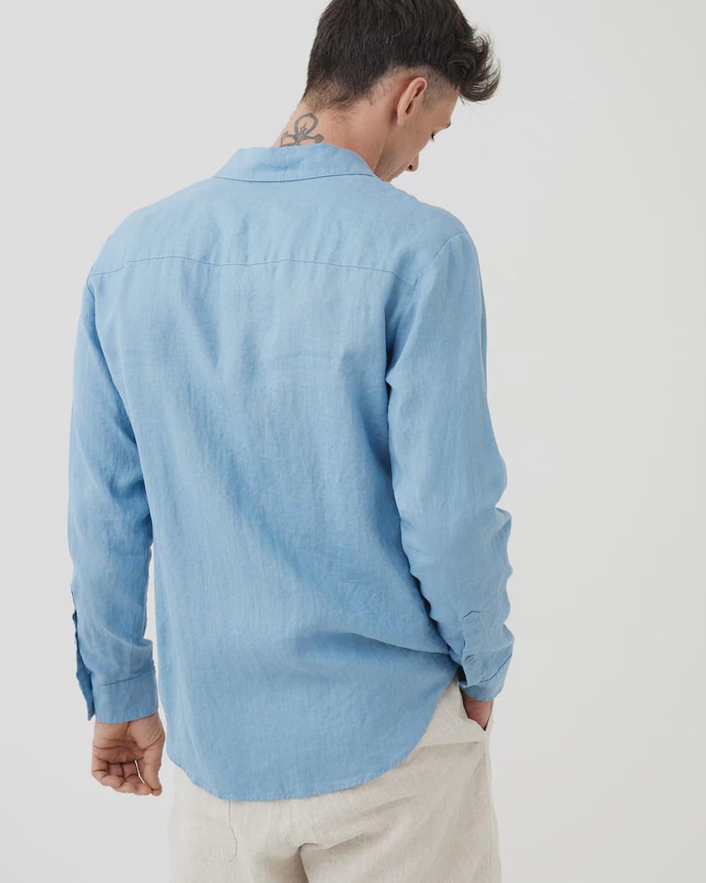 Pu&ograve; includere: Camicia azzurra a maniche lunghe con colletto classico e polsini con bottoni. La camicia &egrave; realizzata in tessuto leggero. Il modello indossa pantaloni beige. La camicia &egrave; tinta unita.