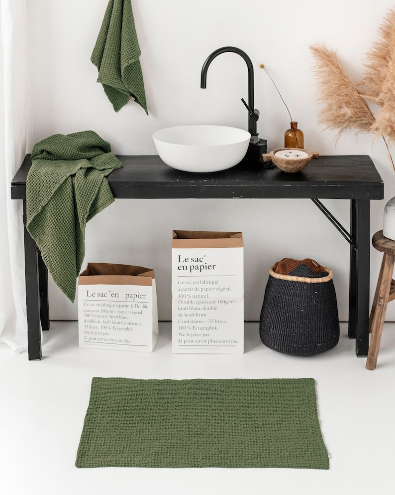 May include: Two brown paper bags with the text "Le sac en papier" on them. The bags are sitting on a black table with a white sink and a green towel. The text on the bags says that they are made from 100% natural paper and have a capacity of 33 litres.