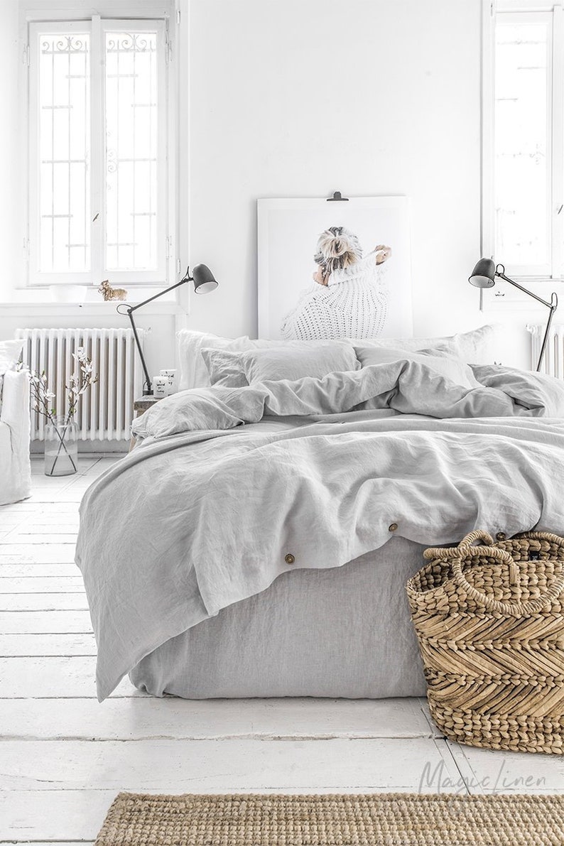 Tranquil bedroom with white painted floor, serene light grey linen bedding and woven textural accents. Magic Linen on etsy.