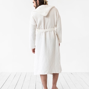 May include: A white waffle weave robe with a hood and a tie belt. The robe is made of a soft, comfortable material and is perfect for lounging around the house.