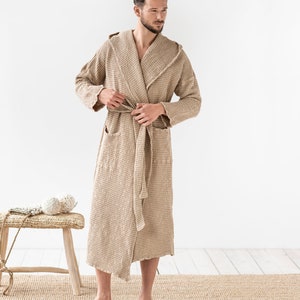 May include: A beige waffle weave robe with a hood and a self-tie belt. The robe is made of a soft, comfortable fabric and has a relaxed fit.