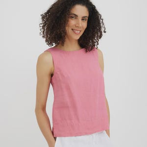 May include: A sleeveless, dusty rose-colored top. The top has a round neckline and a slightly boxy fit. The model is wearing the top with white pants. The background is a plain white.