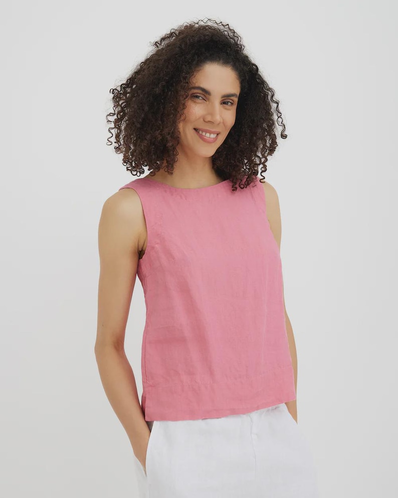 May include: A sleeveless, dusty rose-colored top. The top has a round neckline and a slightly boxy fit. The model is wearing the top with white pants. The background is a plain white.