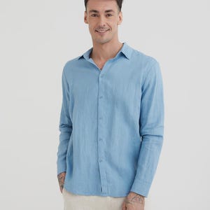 Pu&ograve; includere: Camicia azzurra a maniche lunghe con chiusura a bottoni. La camicia &egrave; realizzata in un tessuto leggero e ha un colletto classico. Il modello indossa pantaloni beige. La camicia &egrave; un capo versatile per un abbigliamento casual o semi-formale.