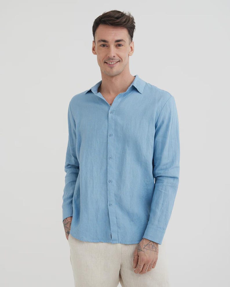 Pu&ograve; includere: Camicia azzurra a maniche lunghe con chiusura a bottoni. La camicia &egrave; realizzata in un tessuto leggero e ha un colletto classico. Il modello indossa pantaloni beige. La camicia &egrave; un capo versatile per un abbigliamento casual o semi-formale.