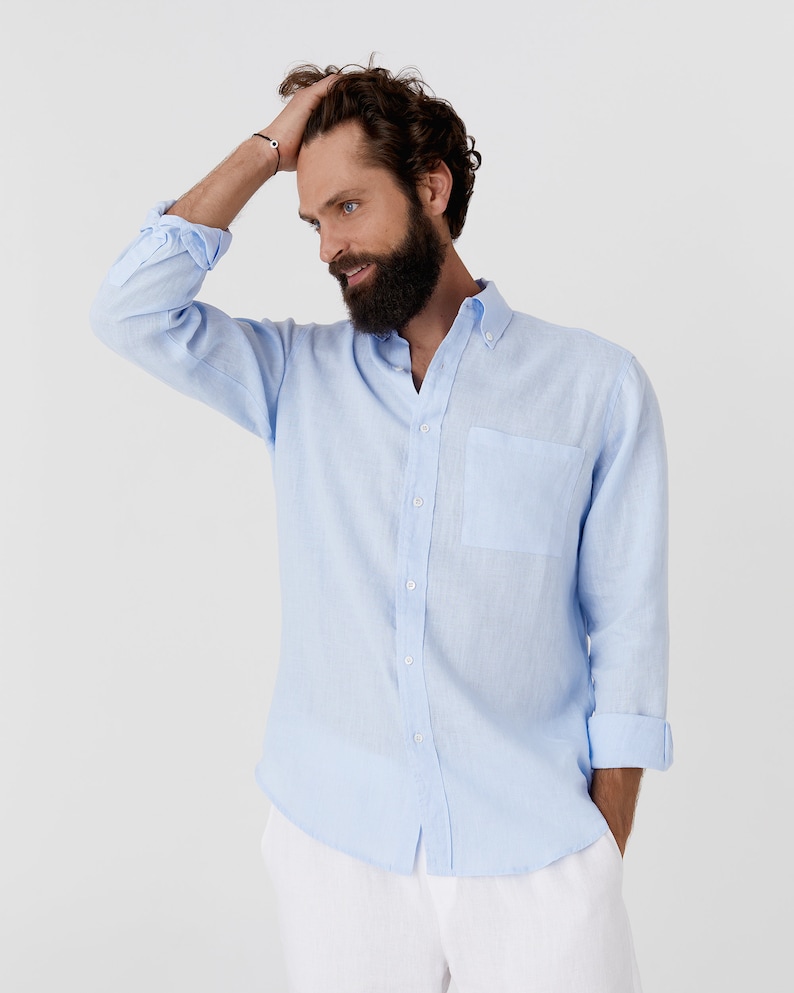 K&ouml;nnte beinhalten: Hellblaues Button-Down-Hemd mit Brusttasche und hochgekrempelten &Auml;rmeln. Das Hemd ist aus leichtem Stoff. Das Model tr&auml;gt eine wei&szlig;e Hose.