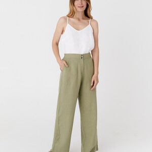 May include: A woman is wearing a white linen tank top and green linen wide-leg pants. She is standing on a white background.