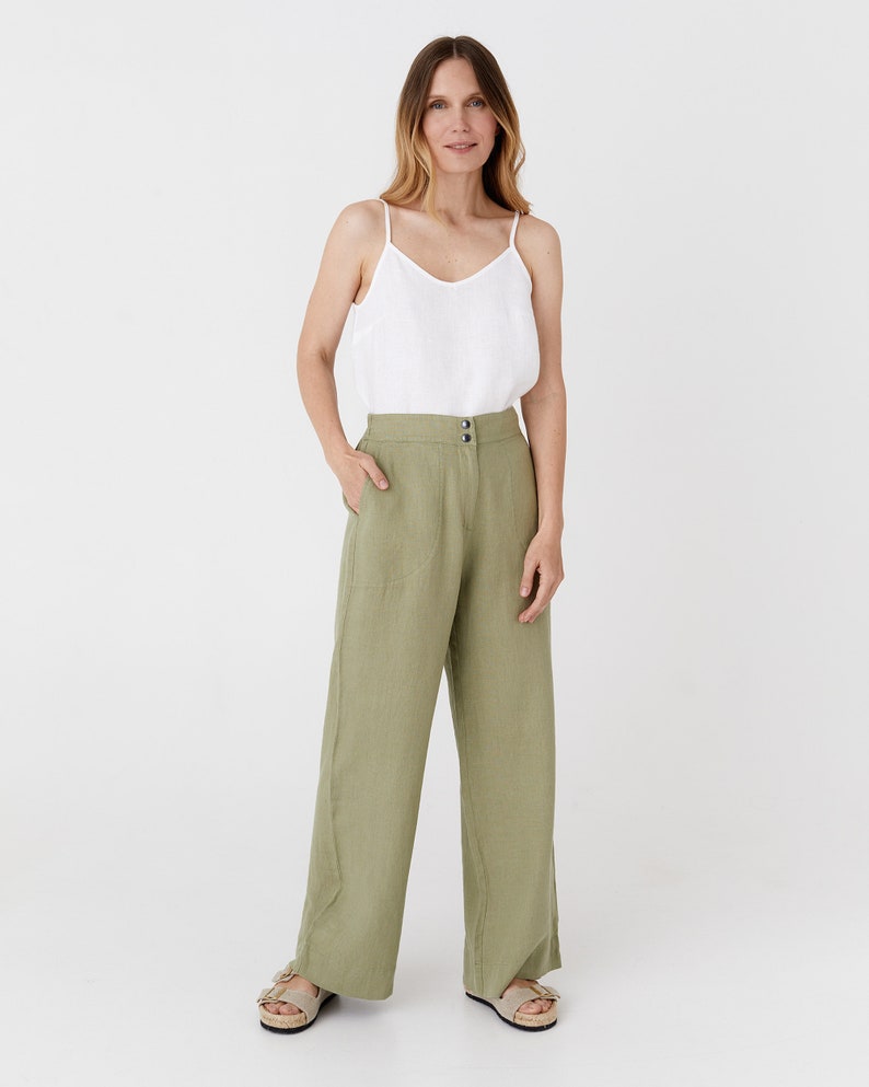 May include: A woman is wearing a white linen tank top and green linen wide-leg pants. She is standing on a white background.