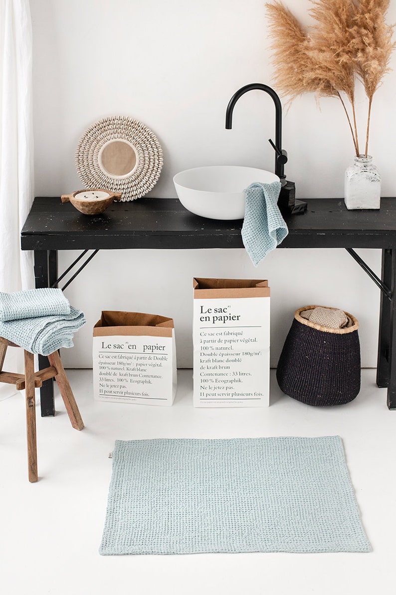 May include: Two brown paper bags with the text "Le sac en papier" printed on them. The bags are sitting on a black table with a white ceramic sink, a blue towel, and a black woven basket. The text on the bags reads: "Ce sac est fabriqu&eacute; &agrave; partir de Double &eacute;paisseur 180g/m&sup2; papier v&eacute;g&eacute;tal. 100% naturel. Kraft blanc doubl&eacute; de kraft brun. Contenance: 33 litres. 100% Ecographik. Ne le jetez pas. Il peut servir plusieurs fois."