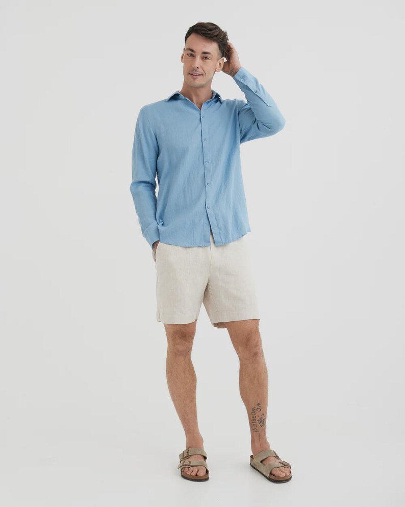 Pu&ograve; includere: Una camicia azzurra a maniche lunghe con bottoni e pantaloncini beige. La camicia &egrave; realizzata in tessuto leggero. I pantaloncini sono al ginocchio. La persona indossa sandali marroni.