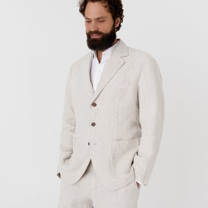 May include: A light beige linen suit jacket with a white button-down shirt underneath. The jacket has a single-breasted closure with four buttons and two flap pockets.
