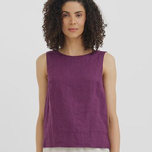 May include: A sleeveless, plum-colored top with a round neckline. The top is made of a textured fabric and has a simple, minimalist design. The model is wearing the top with light-colored pants.