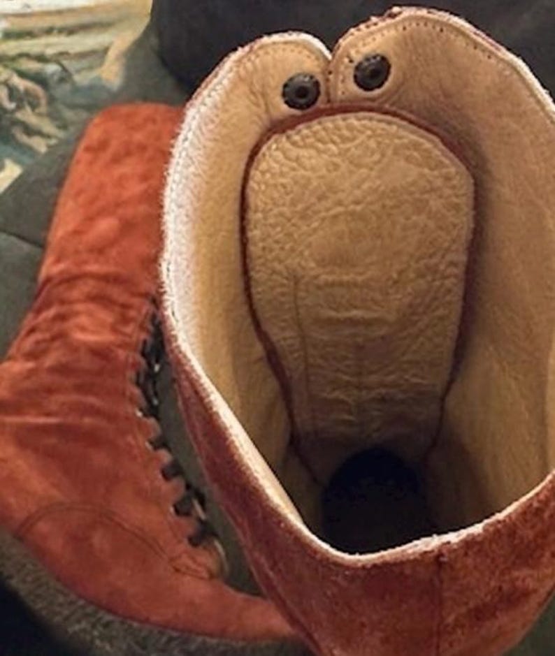 Puede incluir: Primer plano de un par de botas de ante marr&oacute;n rojizo. El interior es de color beige claro con una plantilla texturizada. El borde superior de la bota tiene dos remaches oscuros. Las botas tienen cordones.