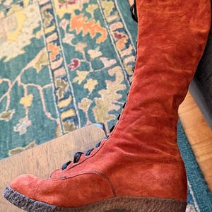 Puede incluir: Una bota alta de ante naranja con cordones negros. La bota tiene una suela texturizada y un tac&oacute;n peque&ntilde;o. La bota es de estilo vintage, probablemente de los a&ntilde;os 70. La bota est&aacute; en buen estado y parece sin usar.