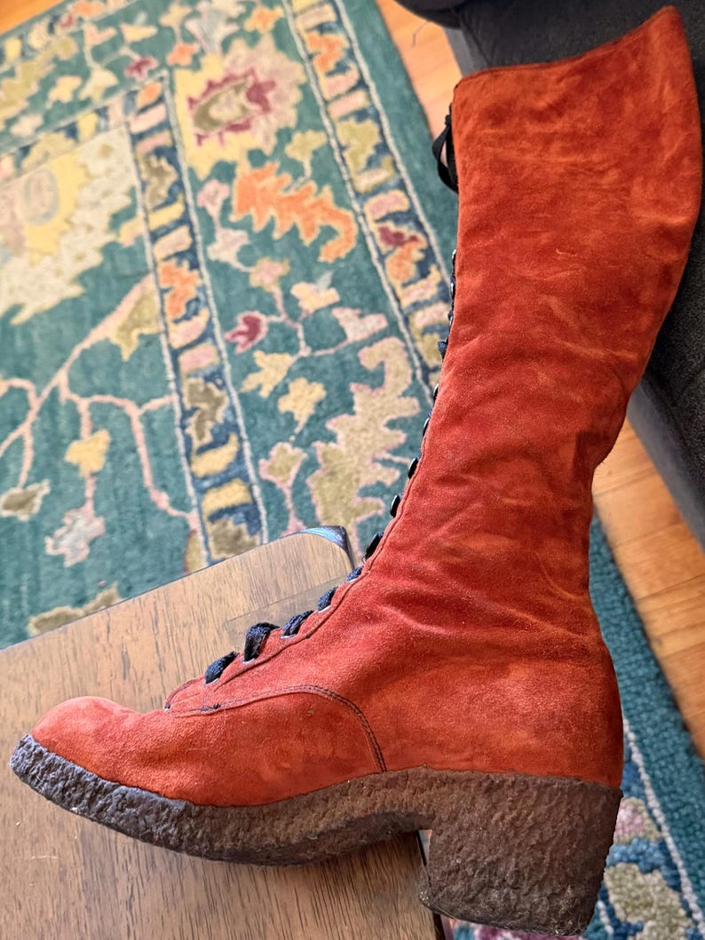 Puede incluir: Una bota alta de ante naranja con cordones negros. La bota tiene una suela texturizada y un tac&oacute;n peque&ntilde;o. La bota es de estilo vintage, probablemente de los a&ntilde;os 70. La bota est&aacute; en buen estado y parece sin usar.