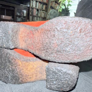 Puede incluir: Primer plano de las suelas de dos zapatos. Las suelas son de color gris claro texturizado con un tal&oacute;n y una puntera gris oscuro. El interior del zapato es naranja. Los zapatos descansan sobre una superficie gris oscuro.