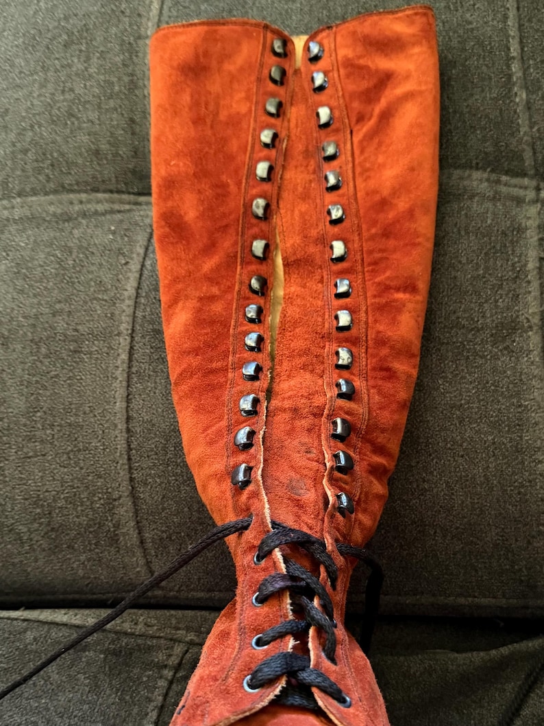 Puede incluir: Una bota alta de ante color &oacute;xido con cordones en la parte delantera. La bota presenta ojales met&aacute;licos y un cord&oacute;n negro. El ante tiene un aspecto ligeramente desgastado. La bota es de estilo vintage.