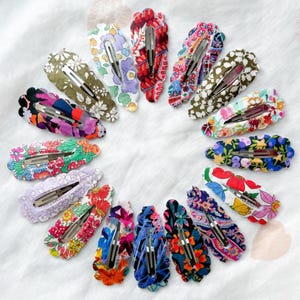 May include: A set of 16 colourful hair clips with floral patterns. The clips are made of fabric and have a scalloped edge.