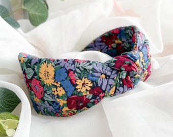 May include: A knotted headband with a floral print featuring red, yellow, blue, and purple flowers on a dark blue background.