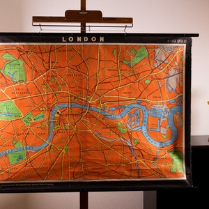 Könnte beinhalten: Vintage London-Karte mit orange-blauen Farbtönen, montiert auf einem Holzrahmen. Die Karte ist oben mit "LONDON" beschriftet. Zwei dekorative gelbe Blumenskulpturen befinden sich rechts von der Karte.