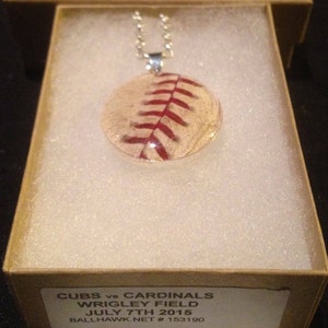 May include: A baseball necklace with a red and white baseball pendant. The pendant is encased in clear resin and features the text "CUBS vs CARDINALS WRIGLEY FIELD JULY 7TH 2015 BALLHAWK NET # 153190".