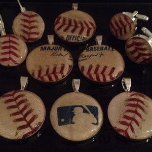 May include: A collection of nine baseball-themed pendants and cufflinks. The pendants feature vintage baseballs with red stitching and various text, including "Major League", "Baseball", and "Official". The cufflinks are also baseball-themed and feature a vintage baseball design.