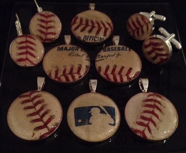 May include: A collection of nine baseball-themed pendants and cufflinks. The pendants feature vintage baseballs with red stitching and various text, including "Major League", "Baseball", and "Official". The cufflinks are also baseball-themed and feature a vintage baseball design.