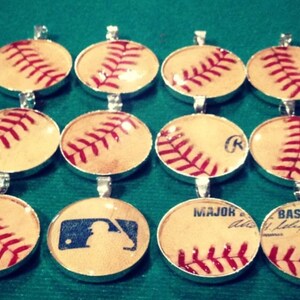 Op de afbeelding: Een verzameling van 10 baseball-hangers, elk met een ander ontwerp. Sommige hangers hebben een baseball met rode naden, terwijl andere een baseball hebben met een speler silhouet of de woorden "Major League Baseball".