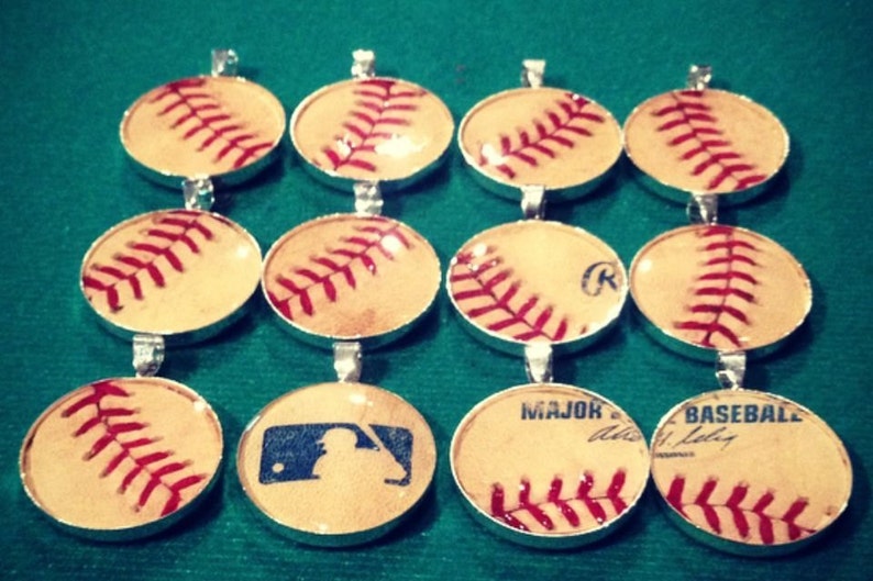 Op de afbeelding: Een verzameling van 10 baseball-hangers, elk met een ander ontwerp. Sommige hangers hebben een baseball met rode naden, terwijl andere een baseball hebben met een speler silhouet of de woorden "Major League Baseball".