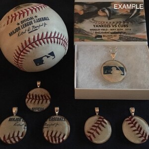 May include: A collection of baseball-themed necklaces. The necklaces feature a variety of baseball designs, including a baseball with the words "Official Major League Baseball" and a silhouette of a baseball player. The necklaces are displayed on a black surface with a white box in the background. The box has the text "Yankees vs Cubs" and "Wrigley Field - May 20th, 2014" on it.