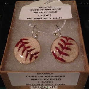 May include: A pair of silver earrings with a baseball-shaped charm. The charms are white with red stitching and a red baseball logo. The earrings are labeled "EXAMPLE CUBS VS MARINERS WRIGLEY FIELD (DATE) BALLHAWK.NET # 123456".