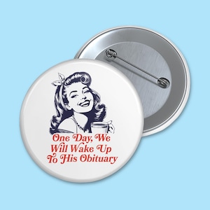 May include: A white button with a retro-style illustration of a woman smiling and holding a cup. The text "One Day, We Will Wake Up To His Obituary" is printed in red on the button.