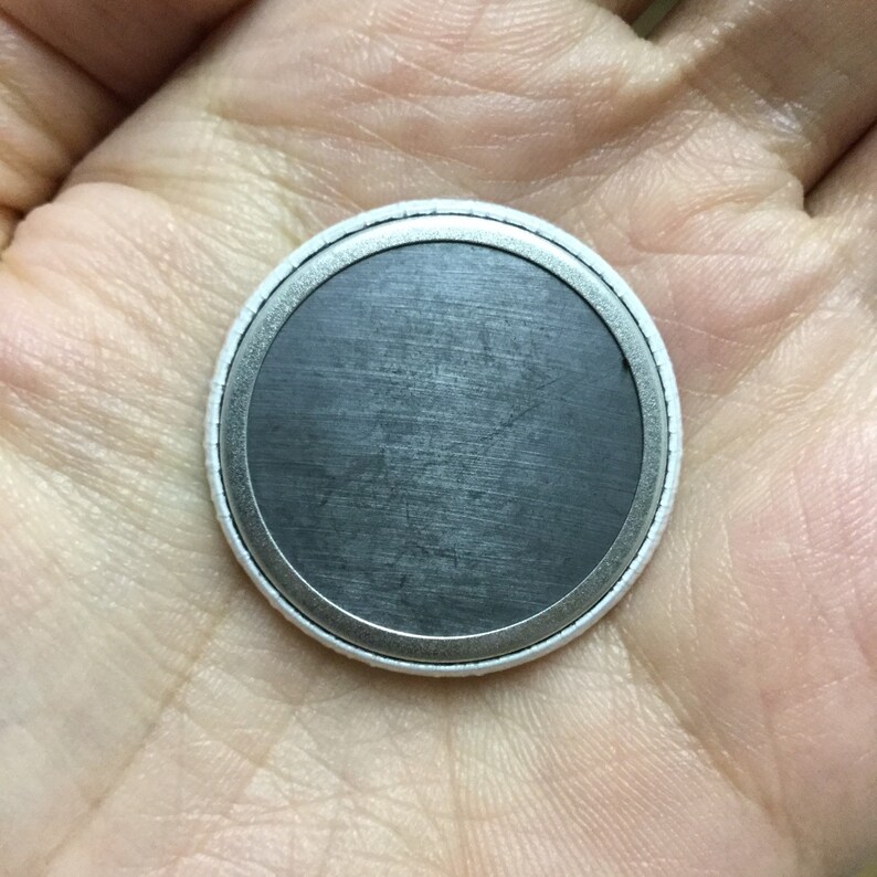 May include: The back of a round, white button with a silver metal rim and a black, magnetic surface.