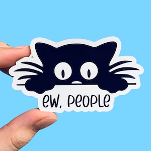 May include: A black cat sticker with the text "ew, people." The cat has large white eyes and is peeking over a white border. The sticker is held against a light blue background.