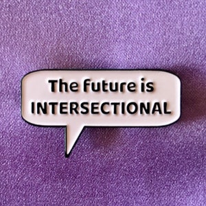 May include: White enamel pin with a black outline in the shape of a speech bubble. The text inside the speech bubble reads "The future is intersectional."