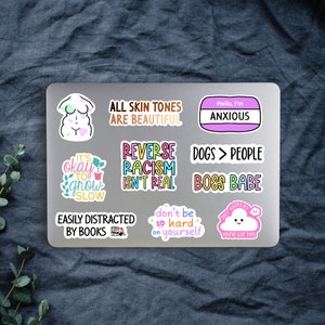 May include: A collection of colorful stickers with various text and graphic designs. The stickers include phrases like "All Skin Tones Are Beautiful," "Hello, I'm Anxious," and "Dogs > People." Other stickers feature illustrations and motivational quotes.