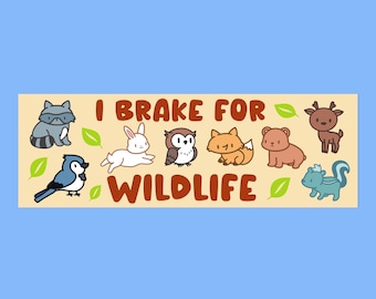 May include: A beige banner with the text "I Brake For Wildlife" in brown letters. The banner features cartoon images of a raccoon, rabbit, owl, fox, bear, deer, and a squirrel.