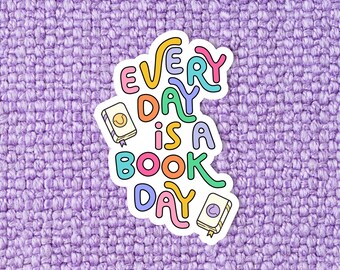 May include: A white sticker with the text "EVERY DAY is a BOOK DAY" in colorful, wavy letters. The sticker is on a purple textured background.