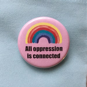 May include: Pink button featuring a rainbow graphic and the text "All oppression is connected".