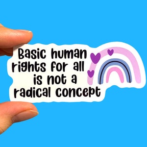 May include: White sticker with the text "Basic human rights for all is not a radical concept" in black text. A rainbow with purple hearts is on the right side of the sticker.