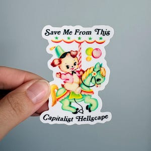 May include: A die-cut sticker featuring a vintage-style illustration of a cream-colored puppy wearing a hat and pink jacket, riding a light green carousel horse. The text reads Save Me From This Capitalist Hellscape in black lettering.