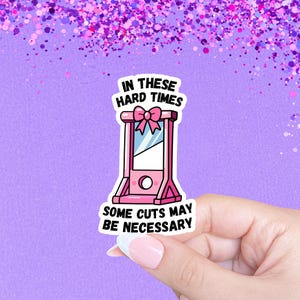 May include: A pink sticker with a cartoon guillotine and the text "In these hard times some cuts may be necessary."