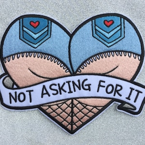 May include: A heart-shaped embroidered patch with a blue denim design and the text "NOT ASKING FOR IT" in black.