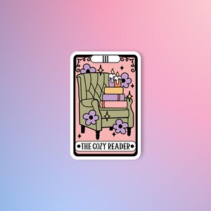 Op de afbeelding: Een roze en witte tarotkaart met een zwarte omtrek. De kaart toont een groene fauteuil met een stapel boeken en kaarsen erop. De kaart is gelabeld met "III THE COZY READER".