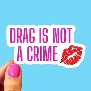 May include: White sticker with pink text that reads "DRAG IS NOT A CRIME" and a red lip print.