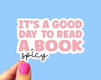 May include: Pink sticker with white outline that reads "It's a good day to read a book" with the word "spicy" written below in black.