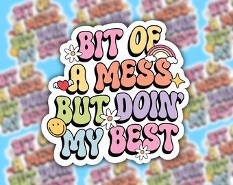 May include: A colorful sticker with the text "Bit of a mess but doin' my best" in a retro font. The sticker features a rainbow, a heart, a star, and flowers.