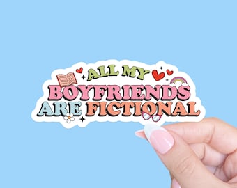 May include: A sticker with the text "ALL MY BOYFRIENDS ARE FICTIONAL" in a retro font. The sticker has a white border and includes illustrations of a book, hearts, a rainbow, a flower, and glasses. The sticker is held by a hand against a light blue background.