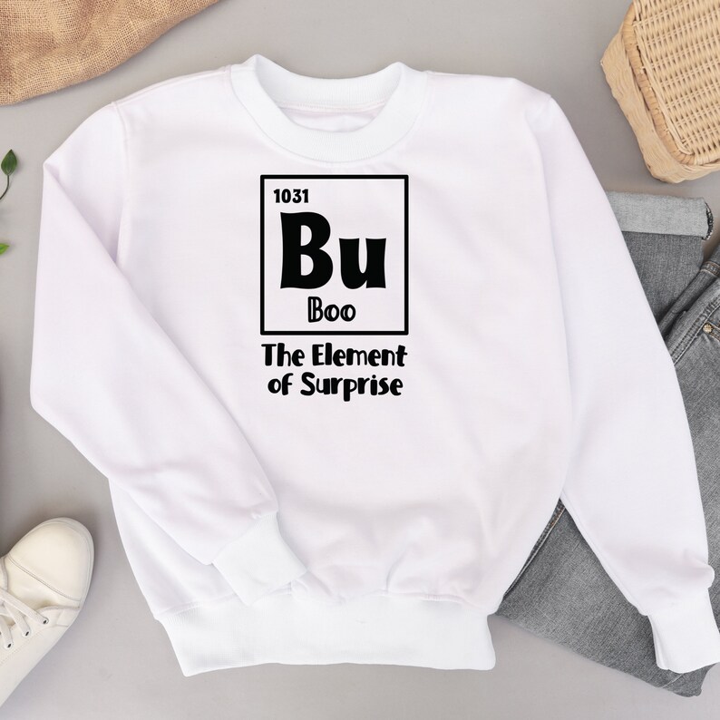 K&ouml;nnte beinhalten: Wei&szlig;er Pullover mit einer schwarzen Grafik eines Elements aus dem Periodensystem. Das Element ist mit "Bu" beschriftet, mit der Ordnungszahl "1031" und dem Namen "Boo". Der Text unter dem Element lautet "The Element of Surprise".