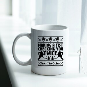 Puede incluir: Taza de caf&eacute; de cer&aacute;mica blanca con un dise&ntilde;o en blanco y negro. El dise&ntilde;o presenta jugadores de hockey y el texto "Making a fist checking you twice".